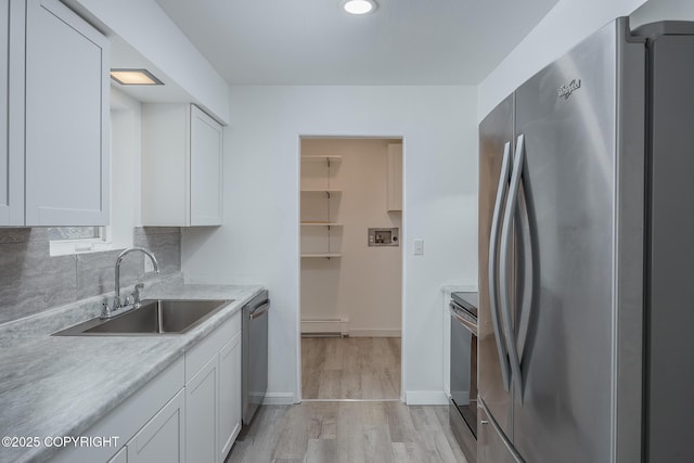 kitchen with a sink, a baseboard radiator, appliances with stainless steel finishes, and white cabinetry