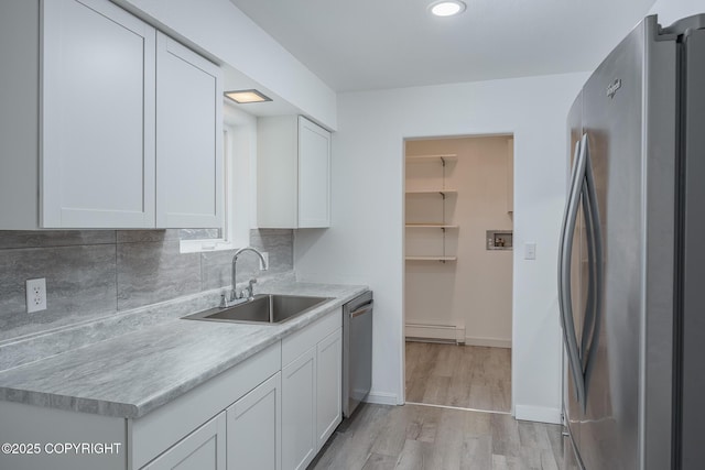 kitchen with a sink, white cabinetry, stainless steel appliances, light countertops, and baseboard heating