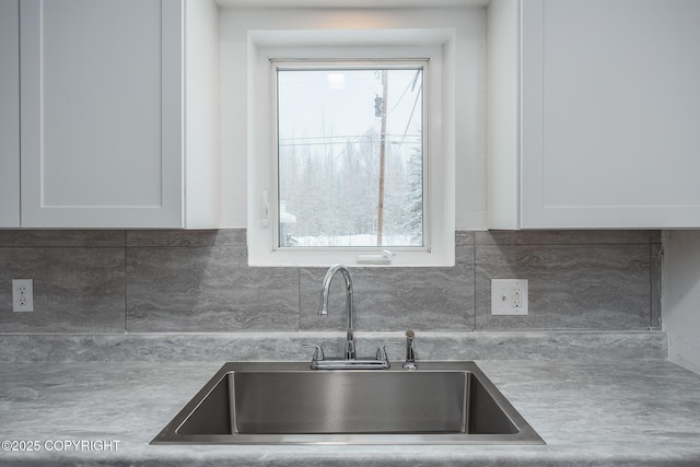 kitchen featuring backsplash, white cabinets, a wealth of natural light, and a sink