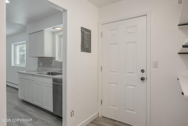 kitchen with a sink, dishwasher, light wood-style floors, a baseboard heating unit, and tasteful backsplash