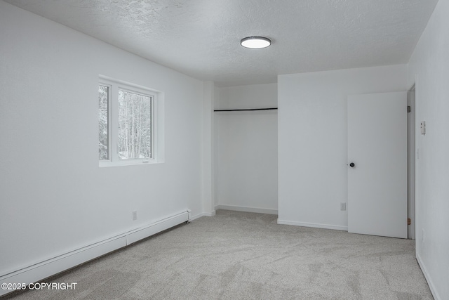 unfurnished bedroom featuring a baseboard heating unit, a textured ceiling, a closet, carpet, and baseboards