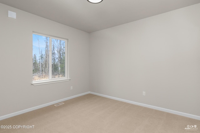 spare room featuring baseboards, visible vents, and light carpet