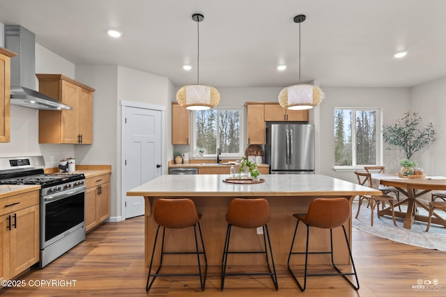 kitchen featuring a healthy amount of sunlight, wood finished floors, stainless steel appliances, wall chimney range hood, and a center island