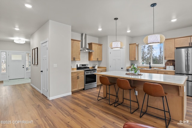 kitchen with a center island, light countertops, wood finished floors, stainless steel appliances, and wall chimney exhaust hood