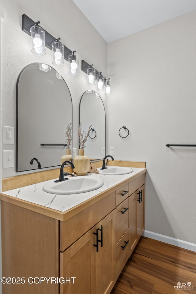 bathroom with a sink, baseboards, wood finished floors, and double vanity