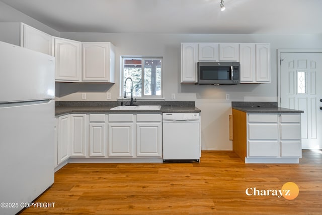 kitchen featuring light wood finished floors, dark countertops, white cabinets, white appliances, and a sink