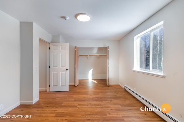 unfurnished bedroom featuring light wood-type flooring, a baseboard radiator, baseboards, and a closet