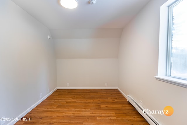 additional living space featuring a baseboard heating unit, baseboards, light wood-style flooring, and vaulted ceiling