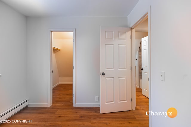 unfurnished bedroom with a baseboard heating unit, baseboards, a walk in closet, and wood finished floors