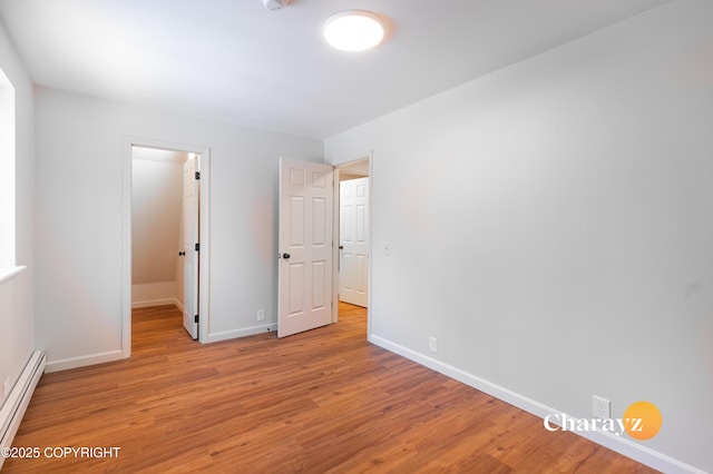 unfurnished bedroom featuring light wood-type flooring, a baseboard radiator, baseboards, and a spacious closet