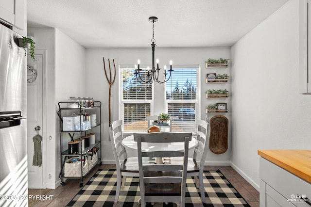 dining space with an inviting chandelier, dark tile patterned flooring, and baseboards