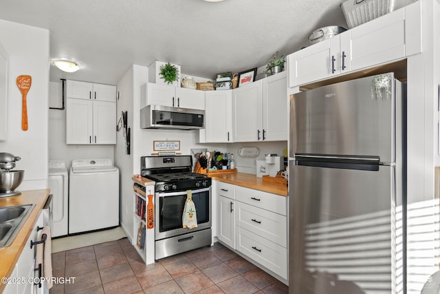 kitchen featuring stainless steel appliances, butcher block countertops, washing machine and dryer, and white cabinets