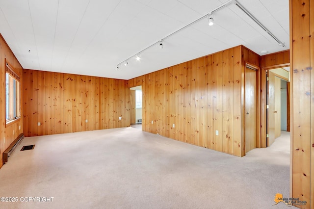 unfurnished room featuring visible vents, track lighting, carpet, wood walls, and a baseboard radiator