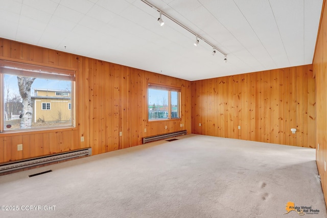 carpeted empty room featuring visible vents, track lighting, a baseboard heating unit, wooden walls, and baseboard heating