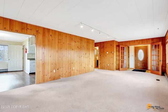 unfurnished living room with rail lighting, carpet flooring, and wood walls