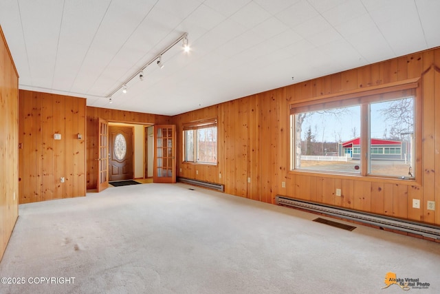 unfurnished living room featuring baseboard heating, carpet flooring, rail lighting, and wood walls