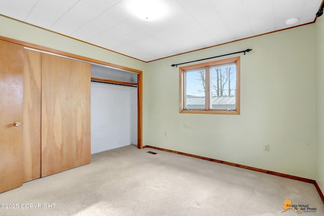 unfurnished bedroom with visible vents, ornamental molding, a closet, carpet floors, and baseboards