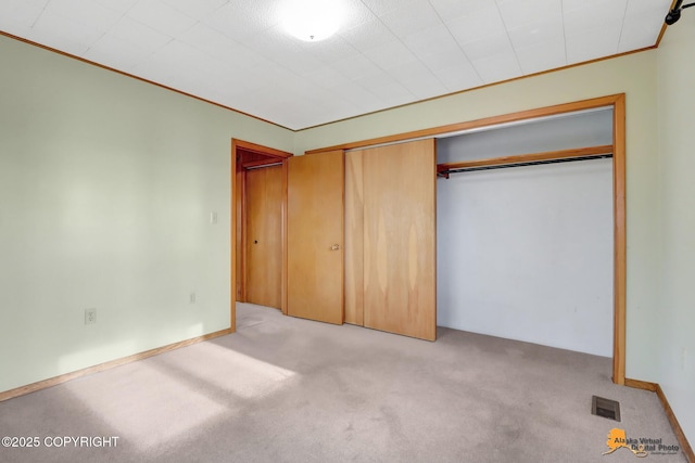 unfurnished bedroom with baseboards, visible vents, ornamental molding, a closet, and carpet flooring