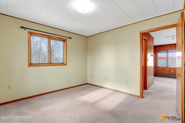 empty room with light colored carpet, a baseboard radiator, baseboards, and ornamental molding