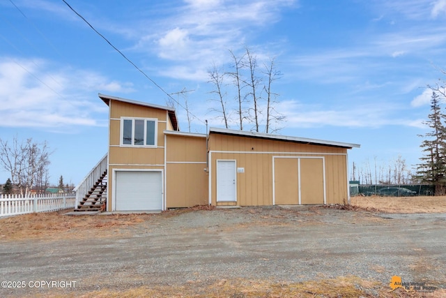 exterior space featuring stairway, dirt driveway, an attached garage, and fence