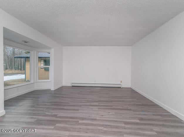 spare room with baseboards, baseboard heating, wood finished floors, and a textured ceiling