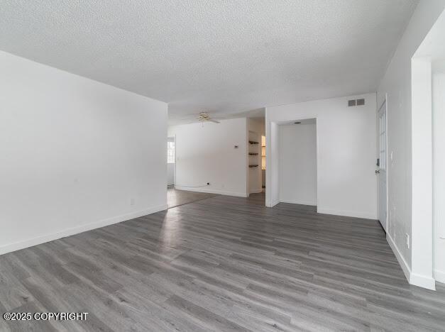 interior space featuring visible vents, a textured ceiling, baseboards, and wood finished floors