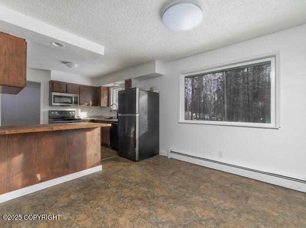 kitchen with butcher block countertops, a baseboard radiator, stainless steel appliances, a textured ceiling, and a sink