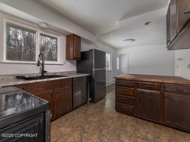 kitchen featuring black appliances, a sink, a textured ceiling, dark brown cabinetry, and butcher block counters