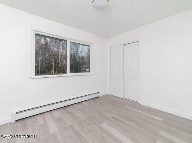 empty room with a baseboard heating unit, baseboards, a textured ceiling, and wood finished floors