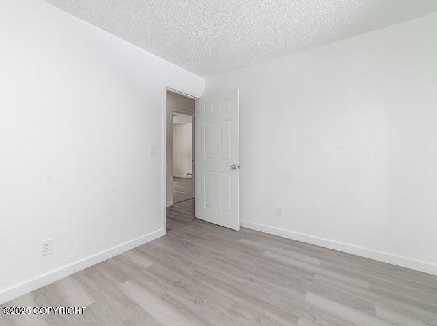 unfurnished room with wood finished floors, baseboards, and a textured ceiling