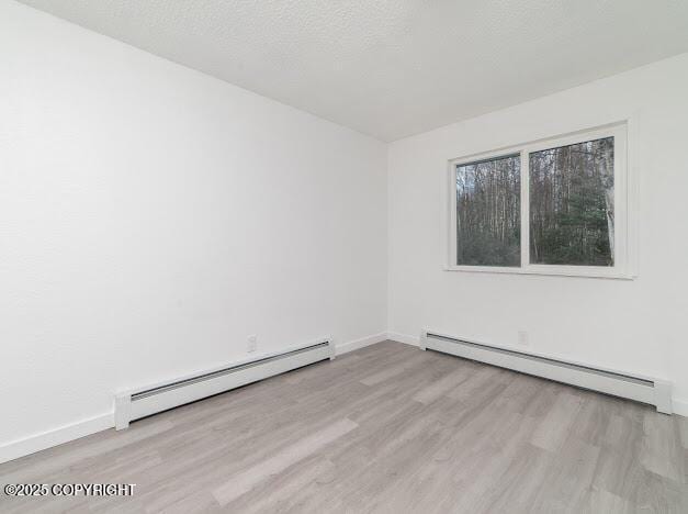 spare room featuring a baseboard heating unit, wood finished floors, baseboards, and a textured ceiling