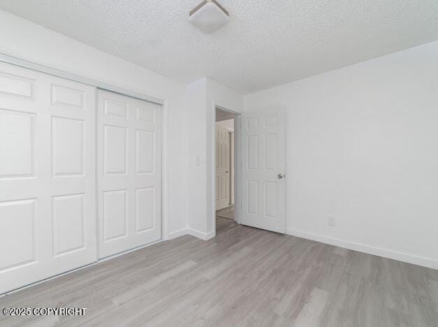 unfurnished bedroom with a closet, a textured ceiling, baseboards, and wood finished floors