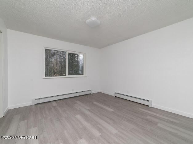 empty room with a textured ceiling, a baseboard heating unit, and wood finished floors