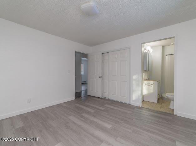 unfurnished bedroom featuring ensuite bathroom, a textured ceiling, wood finished floors, a closet, and baseboards