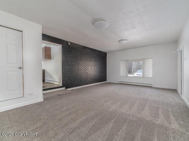 empty room with a baseboard heating unit, carpet flooring, baseboards, and brick wall