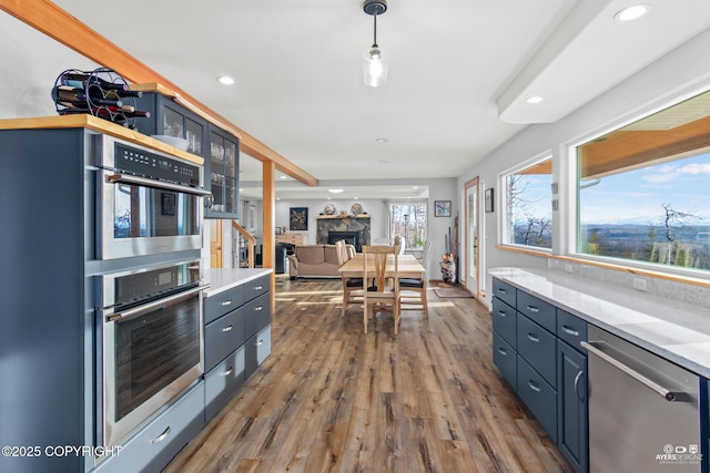 kitchen with a fireplace, wood finished floors, light countertops, and stainless steel dishwasher