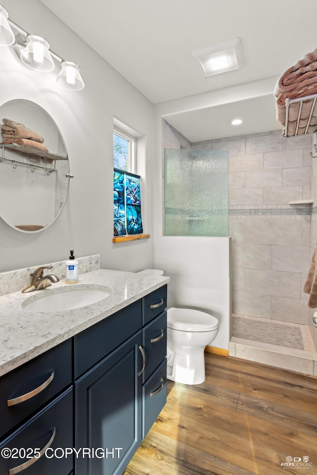 bathroom featuring a walk in shower, toilet, vanity, and wood finished floors