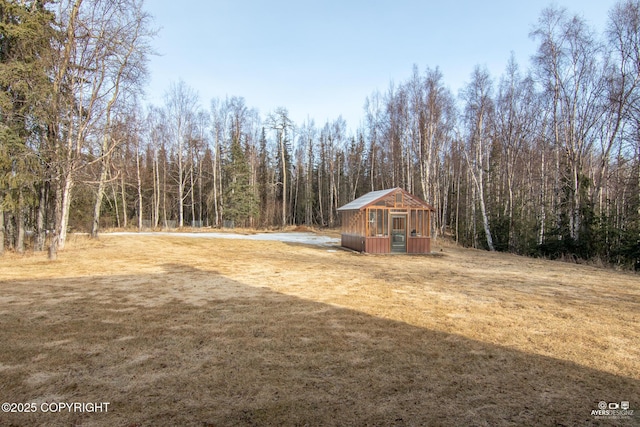 view of yard featuring a greenhouse, an outbuilding, and a wooded view