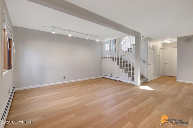 below grade area with a baseboard heating unit, baseboards, stairs, light wood-type flooring, and baseboard heating