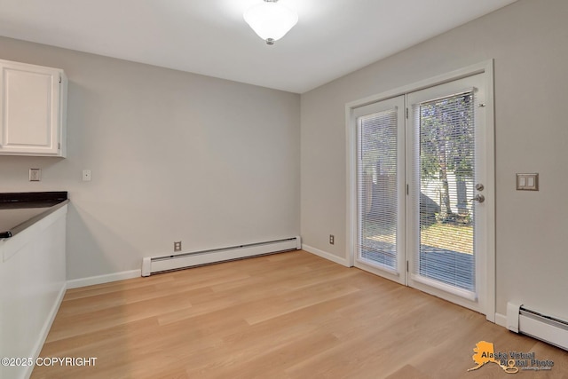 unfurnished dining area featuring a baseboard heating unit, baseboards, and light wood-type flooring