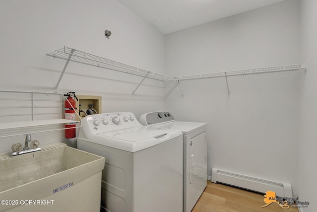 laundry room featuring laundry area, baseboard heating, wood finished floors, washer and dryer, and a sink