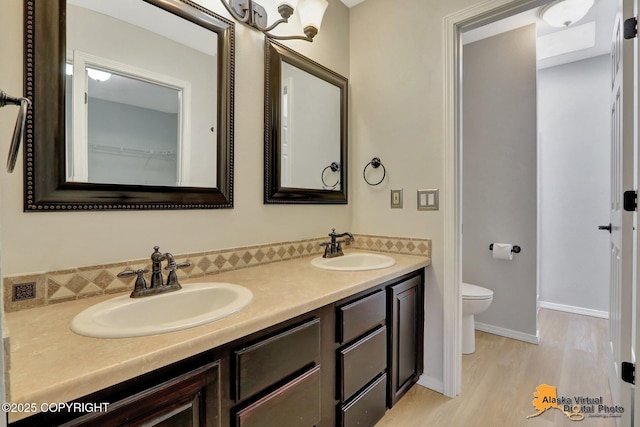 full bathroom with a sink, toilet, wood finished floors, and double vanity