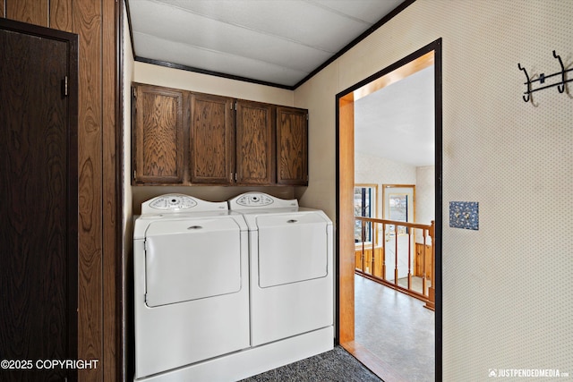 clothes washing area featuring wallpapered walls, cabinet space, and washer and clothes dryer