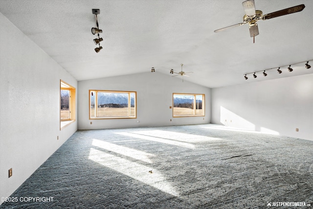 unfurnished living room with lofted ceiling, rail lighting, carpet, and a textured ceiling