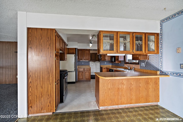 kitchen with light floors, a peninsula, freestanding refrigerator, washing machine and dryer, and brown cabinets