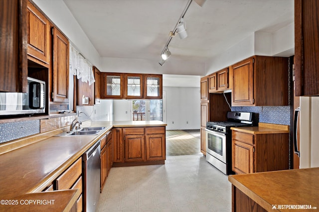 kitchen featuring brown cabinets, a sink, appliances with stainless steel finishes, a peninsula, and light floors