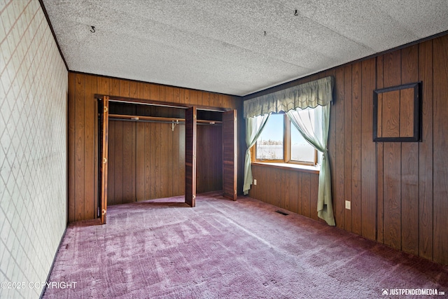 unfurnished bedroom featuring wooden walls, visible vents, carpet floors, a closet, and a textured ceiling