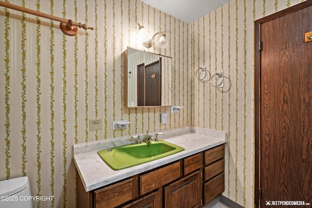 half bath with toilet, wallpapered walls, and vanity