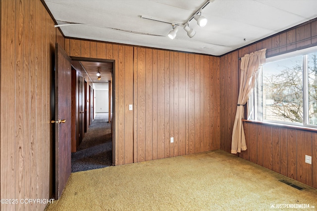 spare room featuring wooden walls, visible vents, track lighting, and carpet