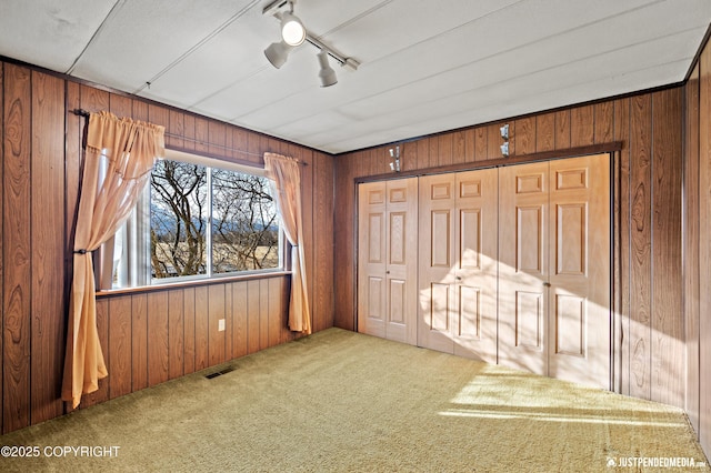 unfurnished bedroom featuring visible vents, track lighting, carpet floors, wood walls, and ceiling fan